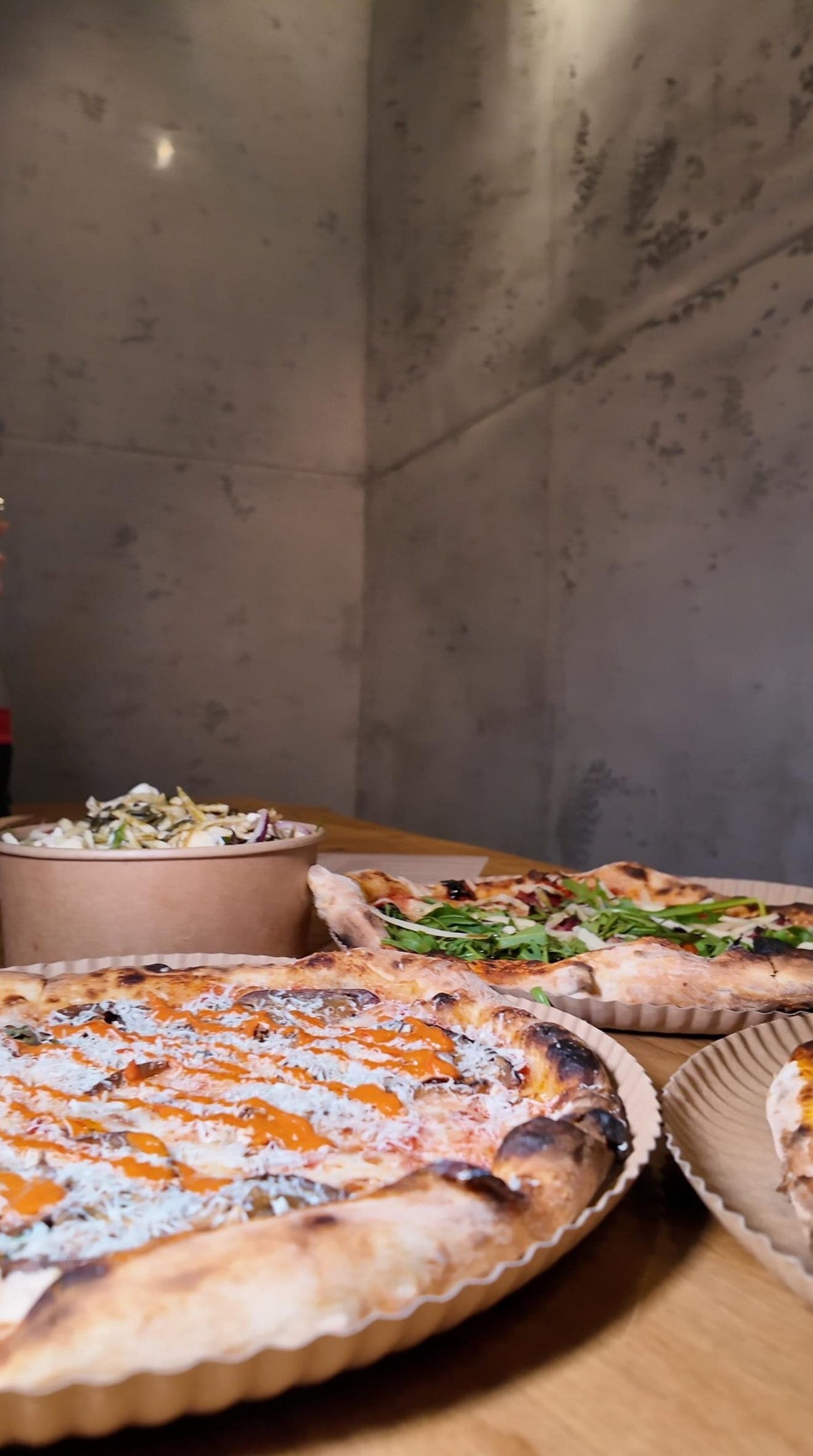 Pizza mit knusprigem Rand, frischem Rucola, cremiger Sauce sowie frischer Salat im Hintergrund bei Zampano To Go Frankfurt