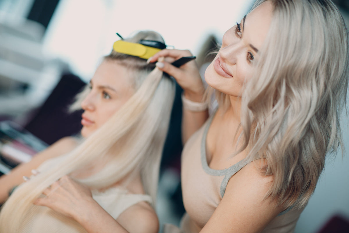 Friseurin arbeitet an einer Echthaarverlängerung bei einer Kundin mit langen blonden Haaren