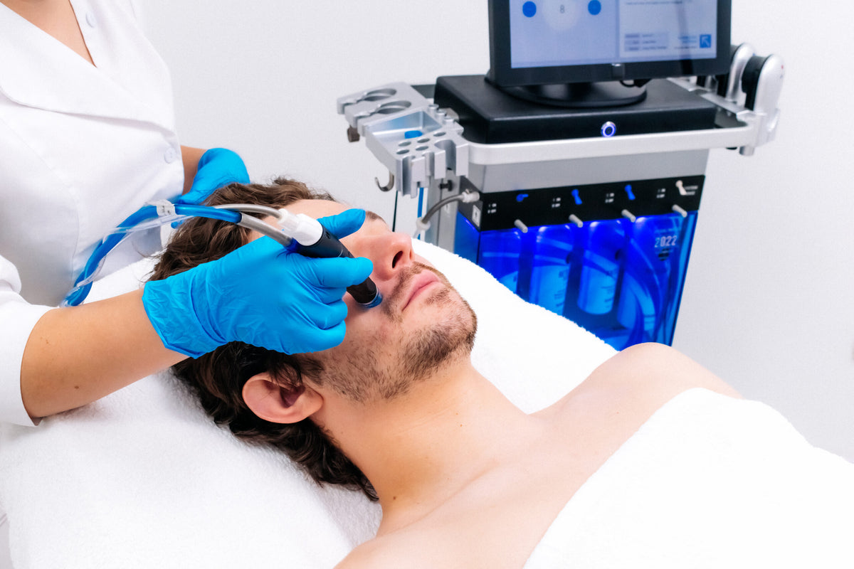 Mann liegt entspannt auf der Behandlungsliege und erhält eine Aqua Facial Behandlung mit modernem Gerät, durchgeführt von einer Fachkraft mit blauen Handschuhen