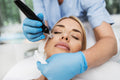 Frau erhält eine Microneedling-Behandlung mit einem elektrischen Dermapen, durchgeführt von einer Fachkraft mit blauen Handschuhen im Kosmetikinstitut