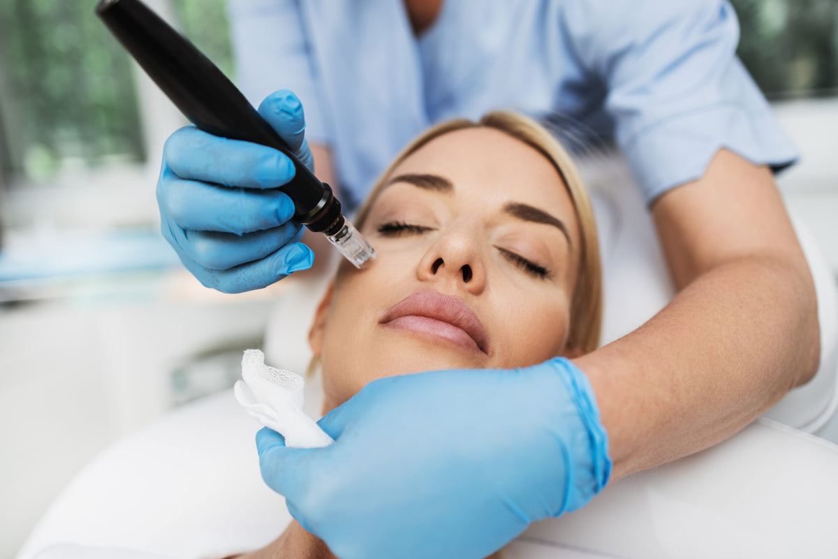 Frau erhält eine Microneedling-Behandlung mit einem elektrischen Dermapen, durchgeführt von einer Fachkraft mit blauen Handschuhen im Kosmetikinstitut