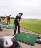 Golfschüler üben konzentriert ihren Abschlag auf der Driving Range der Golfschule Hessen