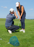 Golflehrer gibt einer Schülerin auf dem grünen Golfplatz Anweisungen zur richtigen Haltung beim Abschlag in der Golfschule Hessen