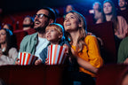 Junge Familie mit Kind sitzt im Kinosessel bei UCI, schaut gespannt auf die Leinwand und hält Popcornboxen in der Hand, umgeben von anderen Besuchern