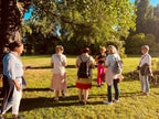 Gruppe von Stadtkrimi-Teilnehmenden im Park bei sonnigem Wetter, diskutieren über Hinweise mit Smartphone und Roadbook in der Hand unter Bäumen