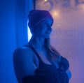 Frau mit Mütze und Sportkleidung steht in der vereisten Kryokammer bei Doctorfrost Frankfurt, umgeben von blauem Licht und kondensierter Kälte an der Glasscheibe