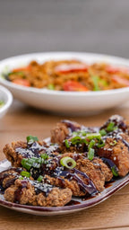 Korean Fried Chicken knusprig glasiert mit Frühlingszwiebeln serviert, im Hintergrund eine passende Beilage bei Der Holländer in Düsseldorf.