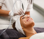 Frau liegt entspannt auf der Behandlungsliege und erhält eine Microdermabrasion im Stirnbereich mit speziellem Gerät durch eine Kosmetikerin in Weiß