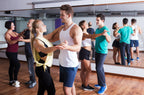Mehrere Paare beim Salsatanzkurs im Tanzstudio, in sportlicher Kleidung vor Spiegelwand, mit lockerer und konzentrierter Stimmung