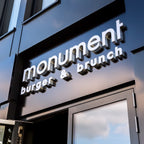 Eingangsbereich von Monument – Burger & Brunch mit modernem Fassaden-Schriftzug in silbernen Lettern auf dunklem Hintergrund