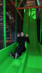 Frau rutscht lachend eine große grüne Rutsche im Indoor-Spielpark von FunFusion Wetzlar hinunter – Action und Spaß im Erlebnisbereich