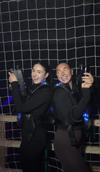 Zwei Spieler mit Lasertag-Westen und Phasern posieren Rücken an Rücken vor einem Netz in der Lasertag-Arena von FunFusion Wetzlar – mit blauen Leuchteffekten