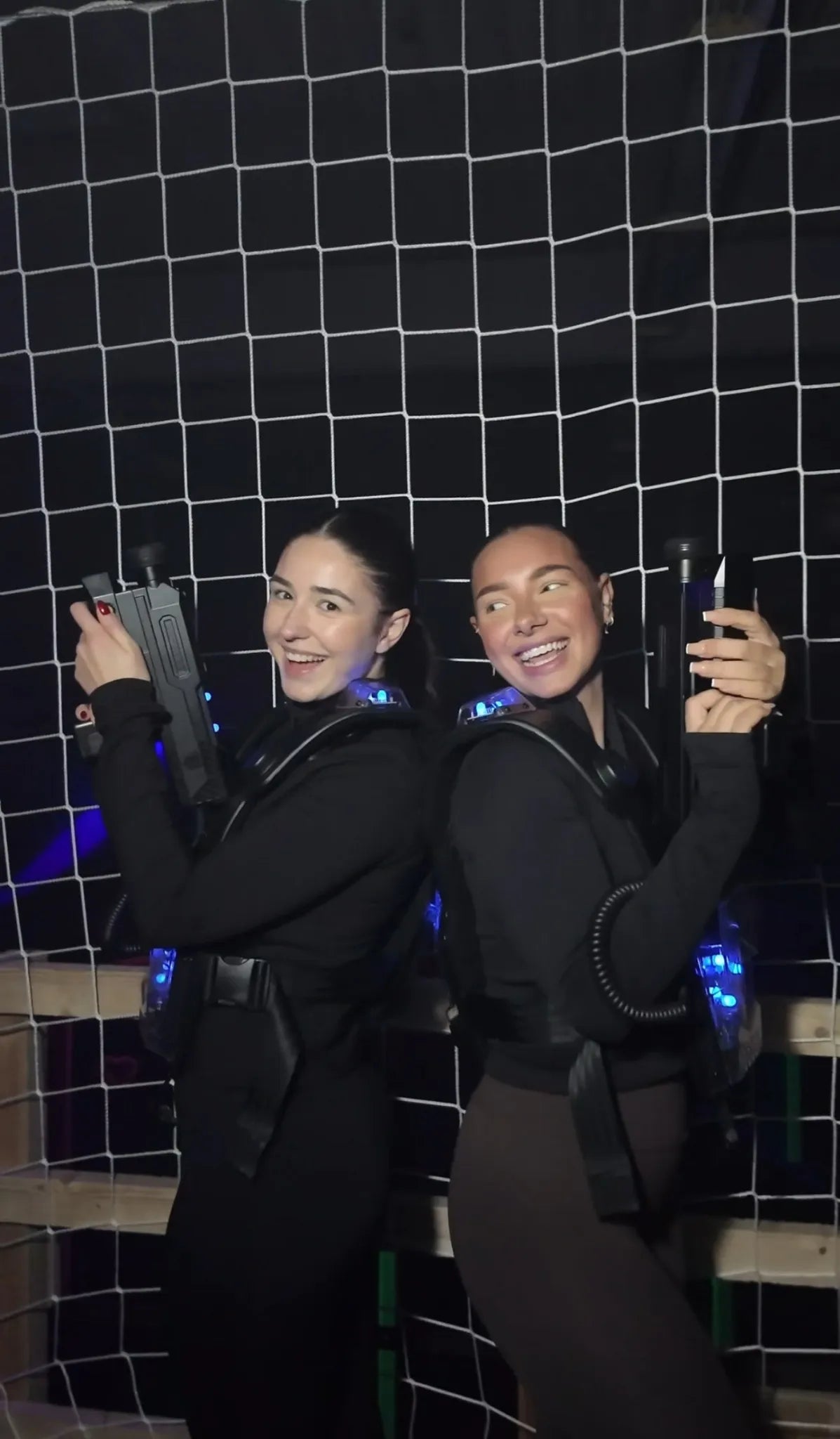 Zwei Spieler mit Lasertag-Westen und Phasern posieren Rücken an Rücken vor einem Netz in der Lasertag-Arena von FunFusion Wetzlar – mit blauen Leuchteffekten