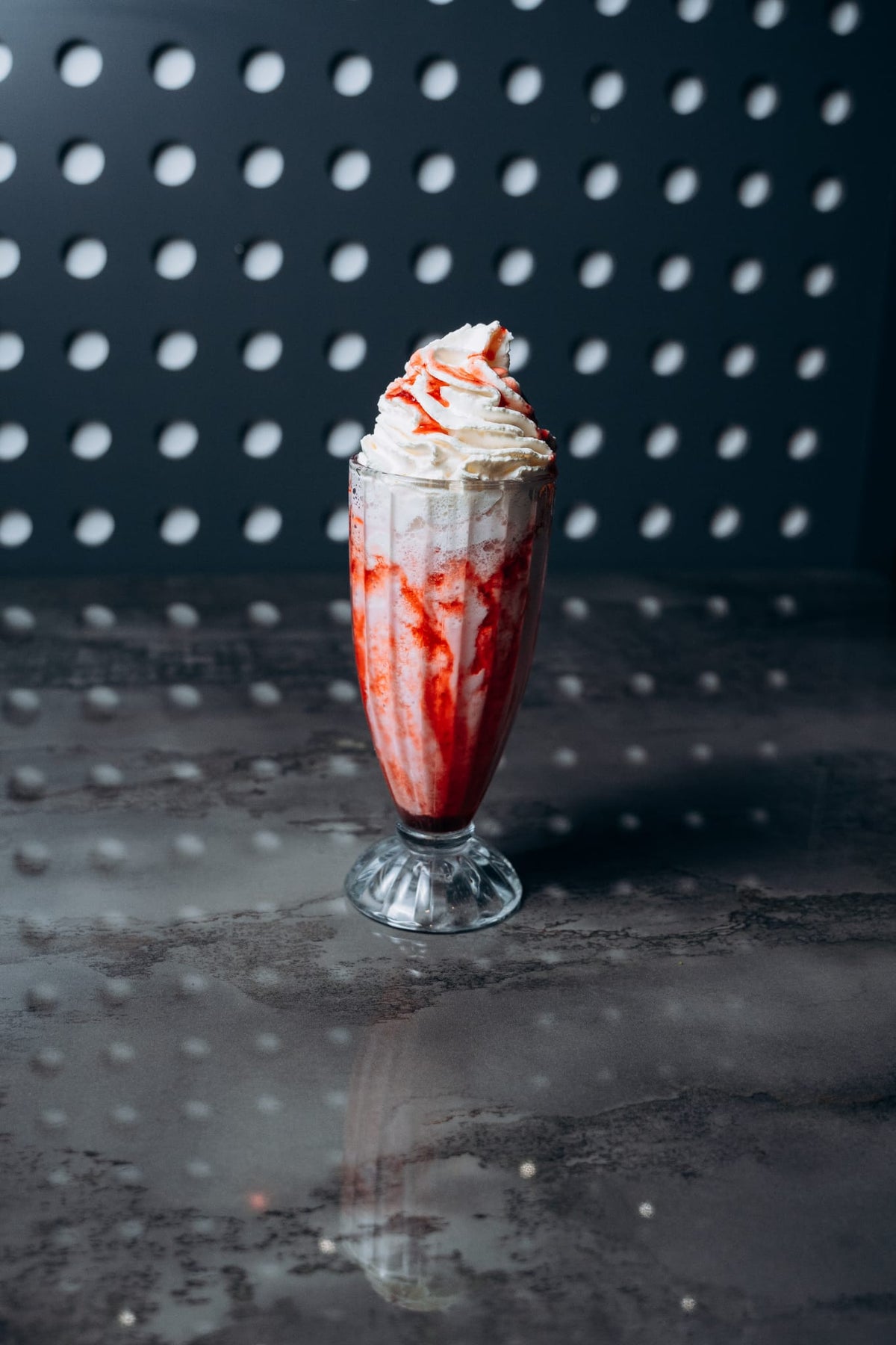 Hoher Erdbeer-Milchshake im Glas, garniert mit Sahnehaube und Erdbeersauce, serviert im modernen Interior von Shiva Food and More Dinslaken
