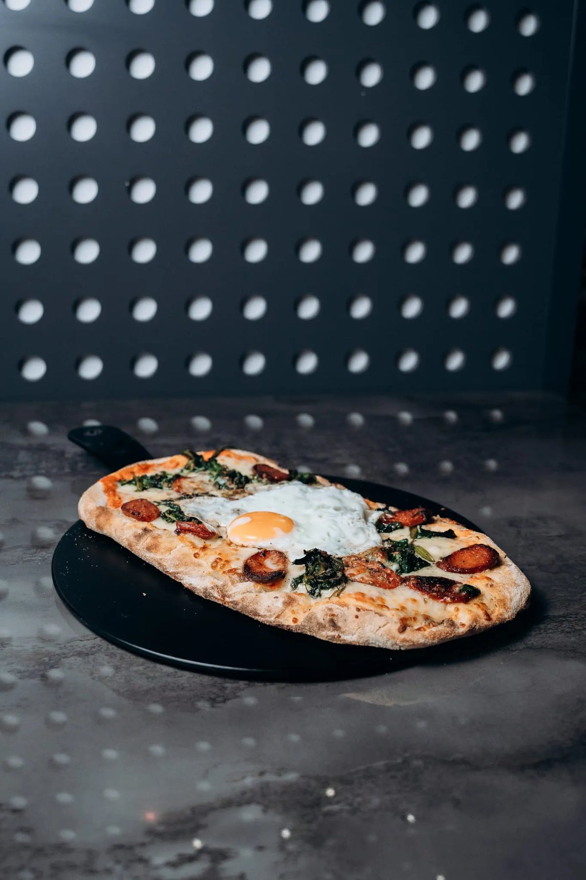 fenfrische Pinsa vom Shiva Food and More Dinslaken, belegt mit Ei, Spinat und Käse, serviert auf schwarzem Teller im modernen Ambiente