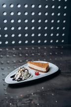 Dessertteller mit Cheesecake, einer Kugel Vanilleeis mit Schokosauce, Sahne und Himbeere, stilvoll angerichtet auf moderner Platte im Shiva Food and More Dinslaken