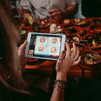 Gast bestellt Tapas über ein Tablet an einem voll gedeckten Tisch bei Tapas & More Dortmund