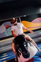 Teilnehmer mit Cowboyhut reitet auf einem mechanischen Bullen bei Face Off Rüsselsheim, im Hintergrund bunte Wandgestaltung im Western-Stil