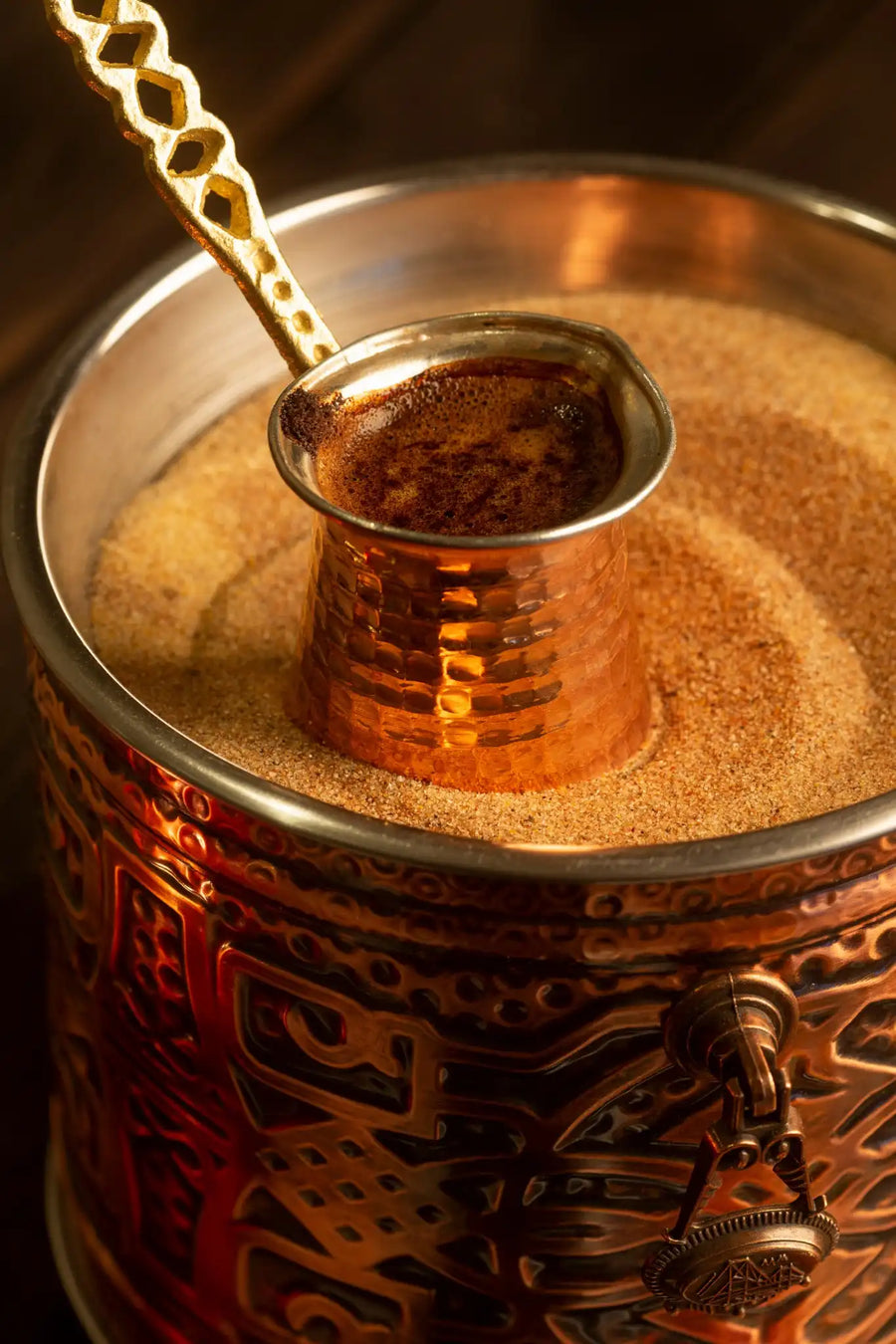 Kupferkännchen mit Schwarztee im heißen Sandbad, aromatisiert mit Kardamom – traditionelle Zubereitung in einem verzierten Gefäß