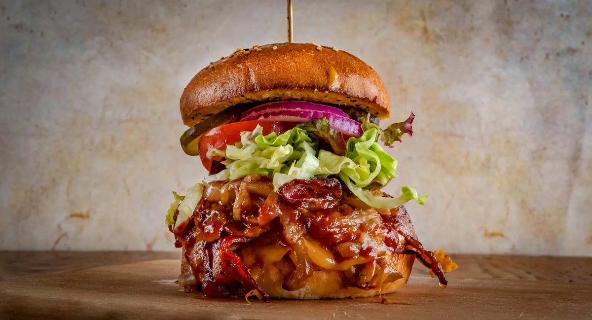 Saloon Hickory Burger aus dem Red Barn BBQ Restaurant mit Pulled Pork, BBQ-Sauce, Käse, Salat, Tomate, Gurke und roten Zwiebeln im Brioche-Bun