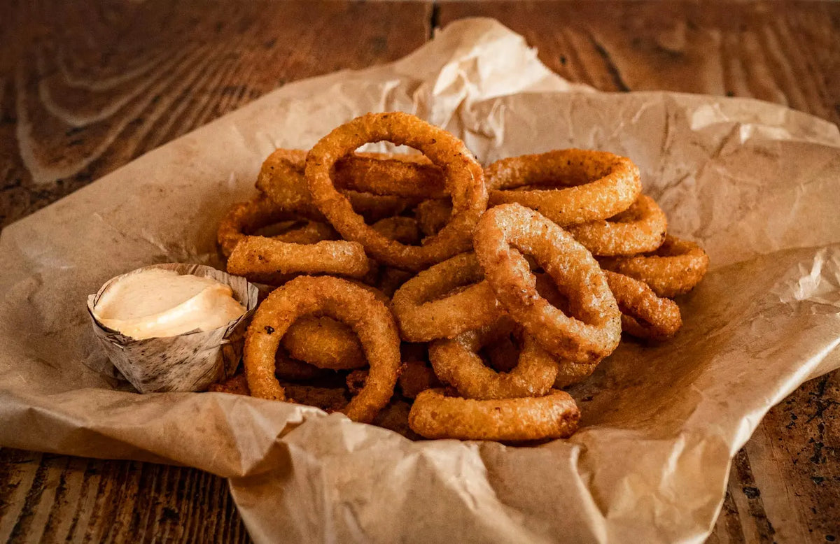 Knusprige Onion Rings vom Red Barn BBQ Restaurant auf Backpapier serviert, dazu ein cremiger Dip auf rustikalem Holztisch