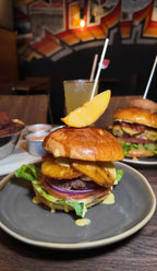 Burger mit gegrillter Ananas, Rindfleischpatty, roten Zwiebeln, Salat und Brioche-Bun, garniert mit Ananasschnitz, im Hintergrund Limonade und weitere Burger im Hornochse Köln