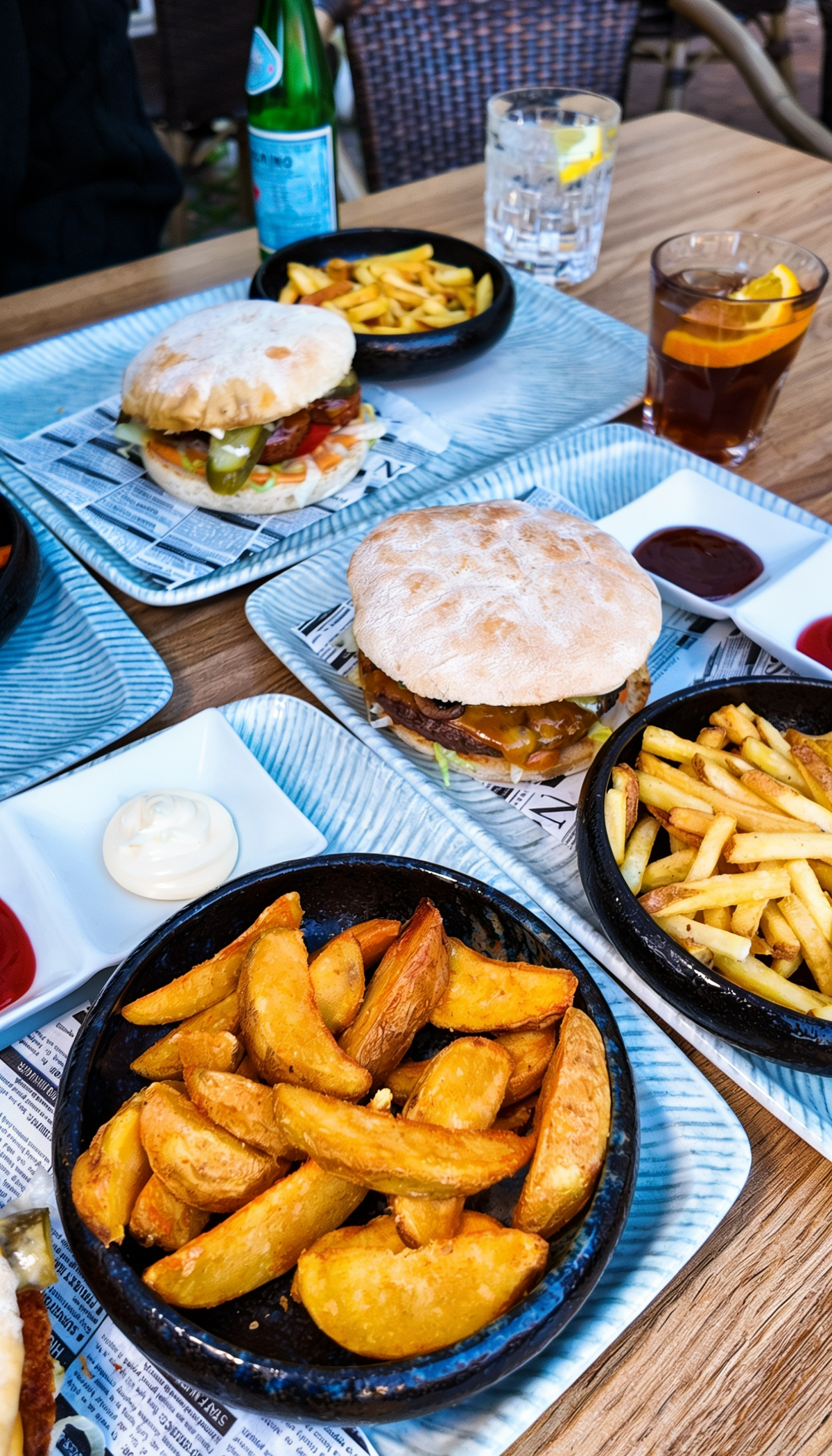 Burger Menüs bei Promis Spritz Cocktail Bar Seligenstadt mit frisch servierten Burgern, Pommes, Kartoffelspalten und verschiedenen Dips auf dem Tisch