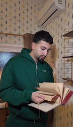 Teilnehmer im grünen Hoodie blättert in einem alten Buch in einem retro eingerichteten Raum – Szene aus dem Escape Room „Muriel_Ingrid“