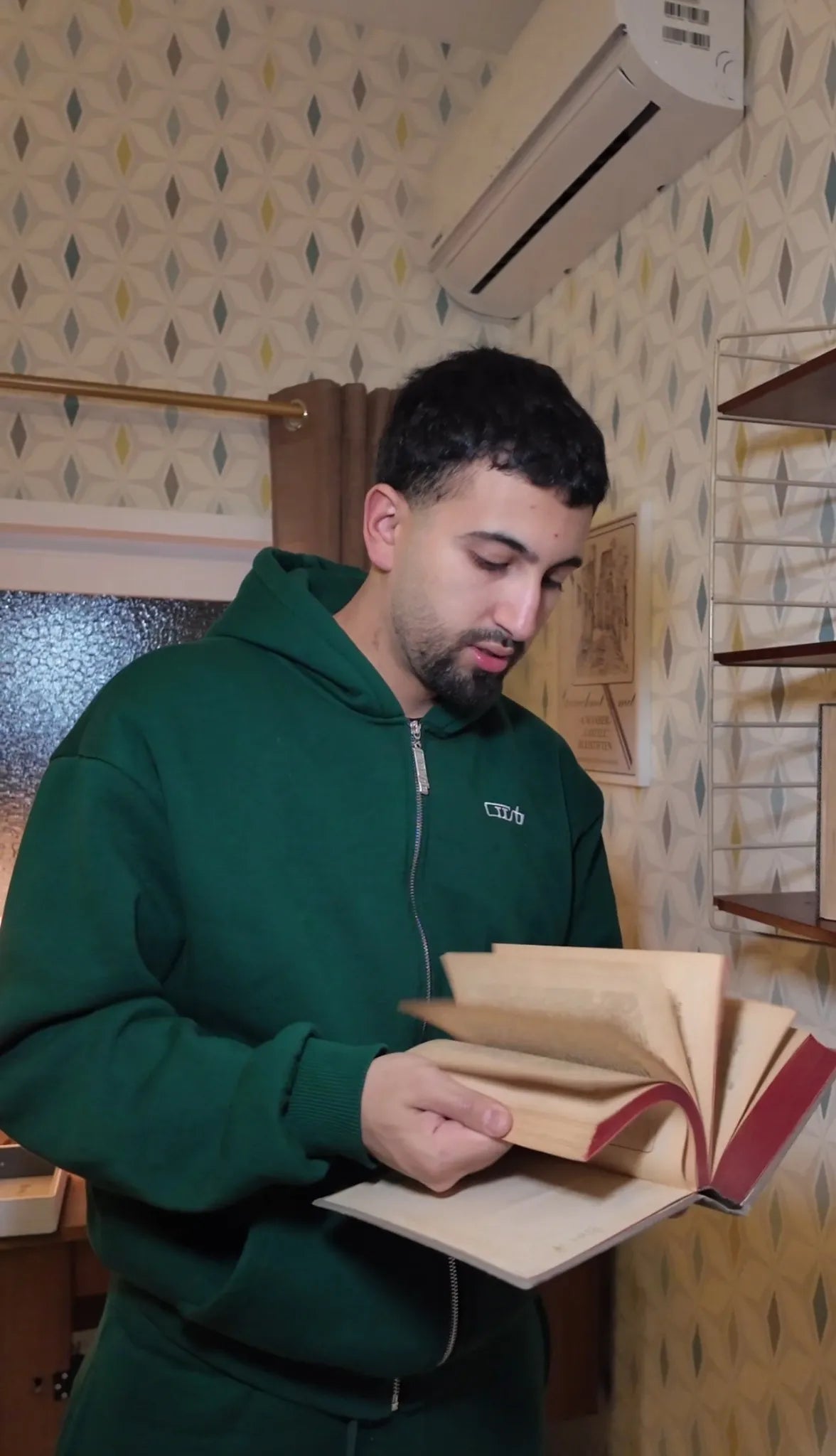 Teilnehmer im grünen Hoodie blättert in einem alten Buch in einem retro eingerichteten Raum – Szene aus dem Escape Room „Muriel_Ingrid“