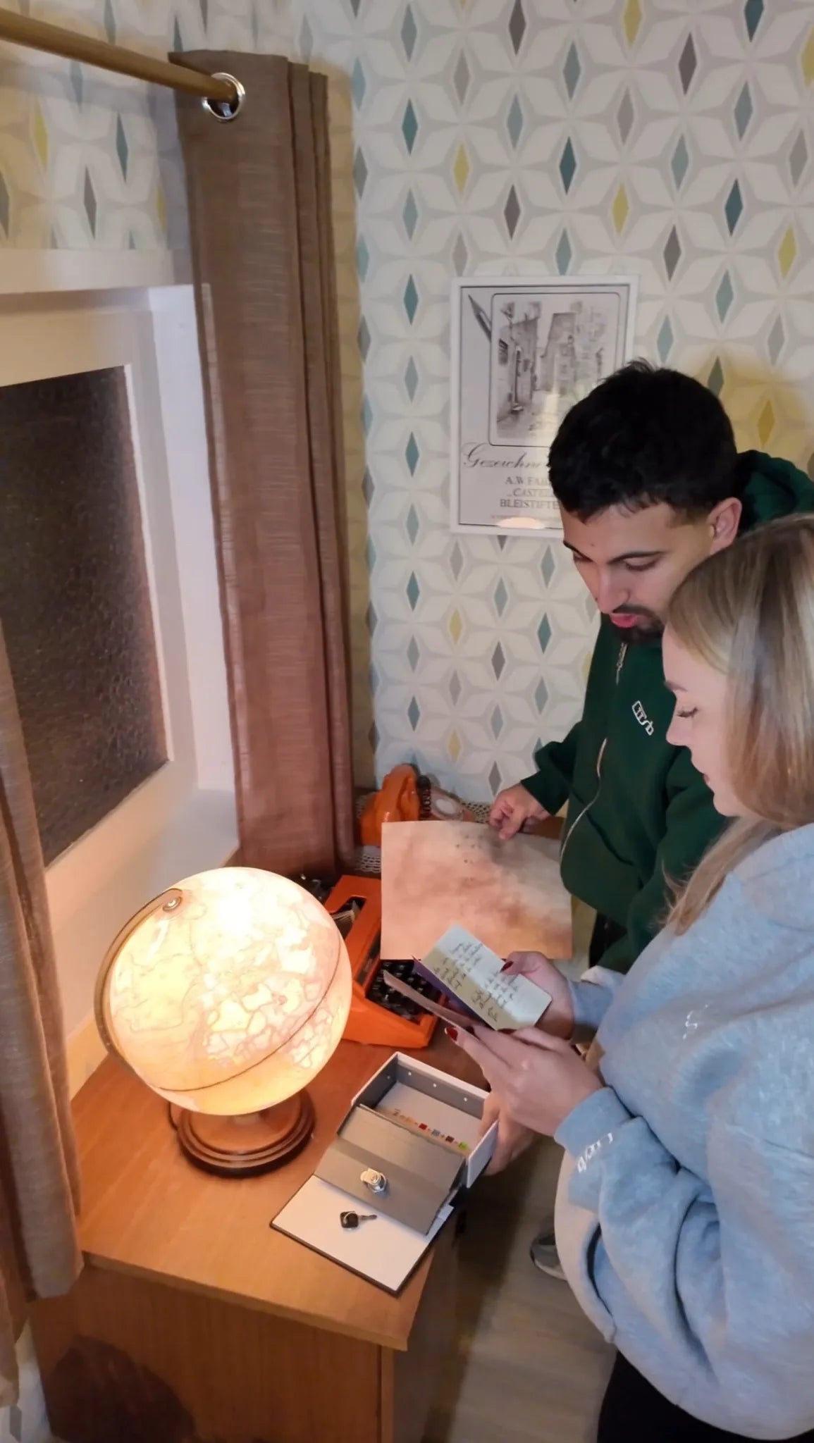 Zwei Personen rätseln im Escape Room „Muriel_Ingrid“ an einem Schreibtisch mit Globuslampe, Schreibmaschine und Karte