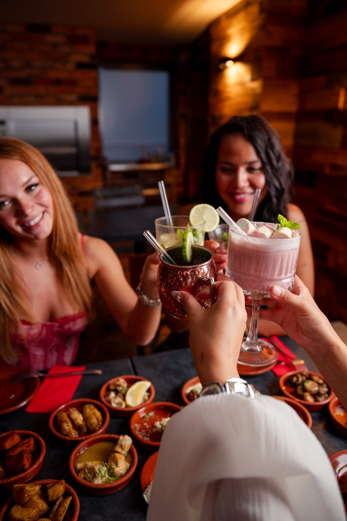 Freundinnen stoßen mit Cocktails im Tapas & More Dortmund an, umgeben von Tapas auf dem Tisch.