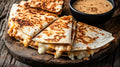 Kross gebratene Käse-Quesadillas auf einem rustikalen Holzbrett, serviert mit einem cremigen Dip im Hintergrund