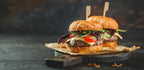 Saftiger Burger mit Rindfleischpatty, Käse, Tomaten, Salat und Gurken auf rustikalem Holzbrett mit Papier serviert