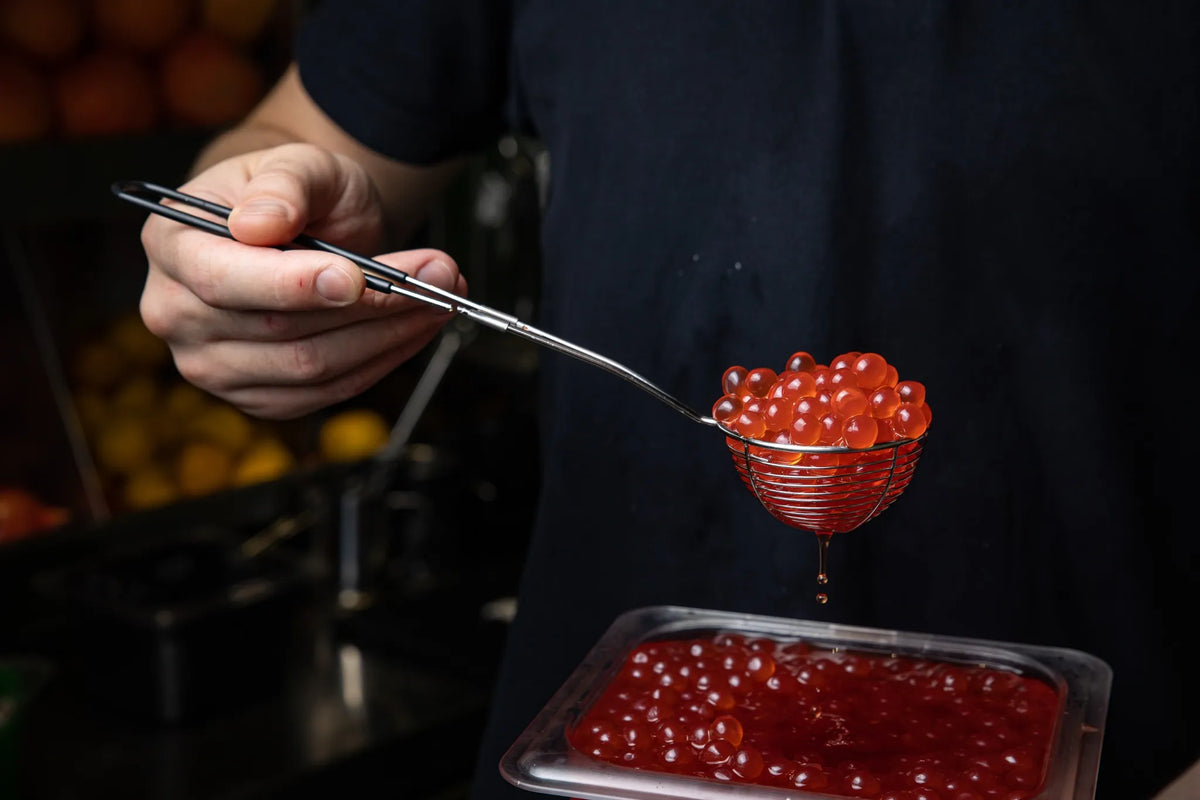 Mitarbeiter schöpft rote Bubble-Tea-Perlen mit einem Sieblöffel aus einem Behälter
