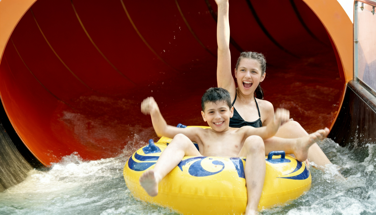 Kinder im gelben Reifen auf einer roten Wasserrutsche im Aqualand Köln während einer spaßigen Fahrt im Erlebnisbad