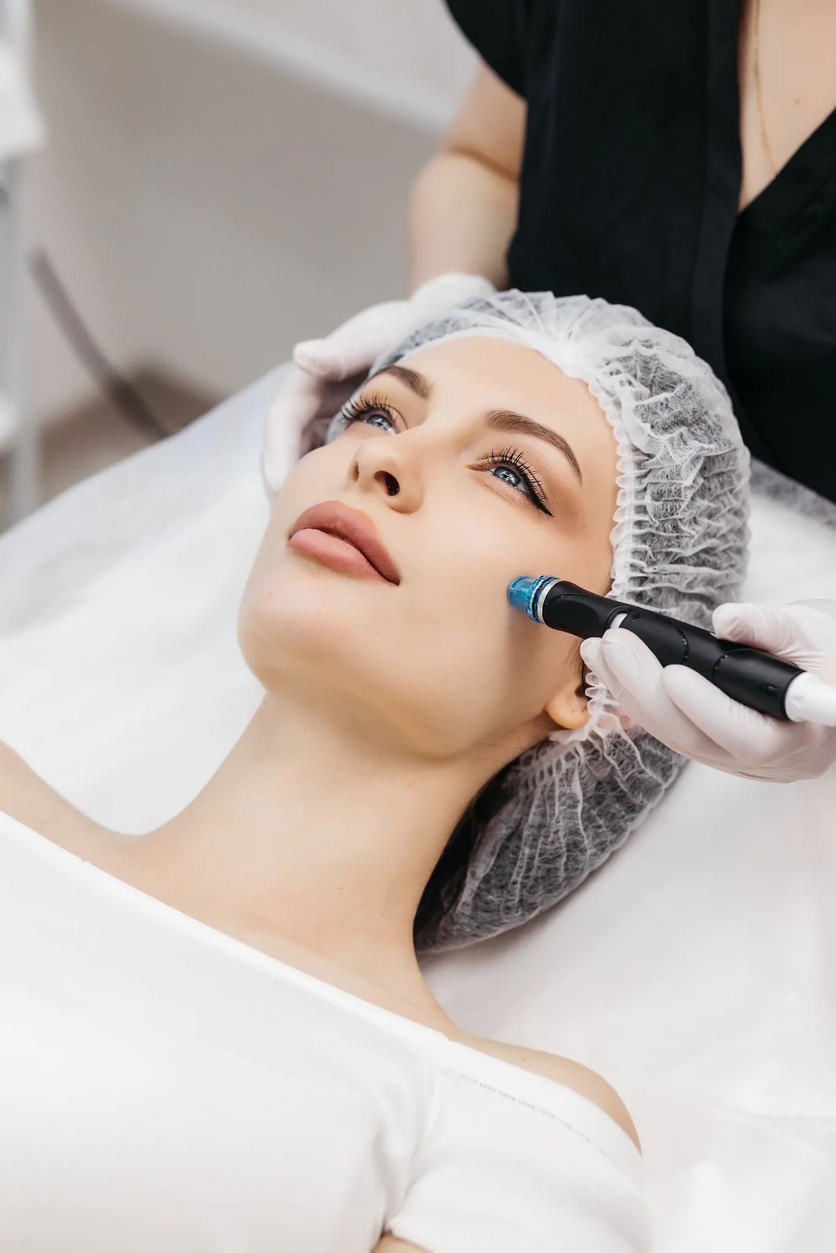 Frau mit Haarnetz erhält eine Aquafacial-Behandlung mit einem speziellen Gerät zur tiefenwirksamen Hautreinigung