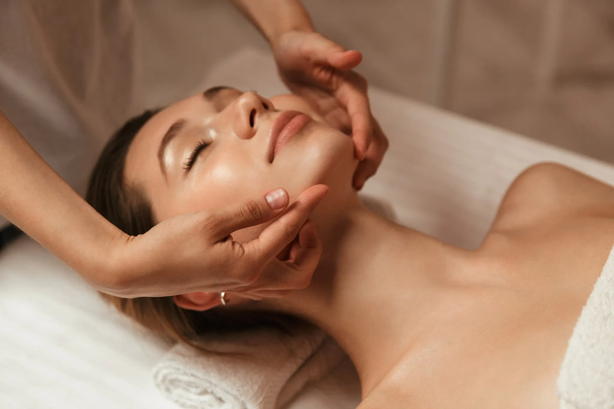 Frau liegt entspannt auf einer Behandlungsliege und erhält eine sanfte Gesichtsmassage