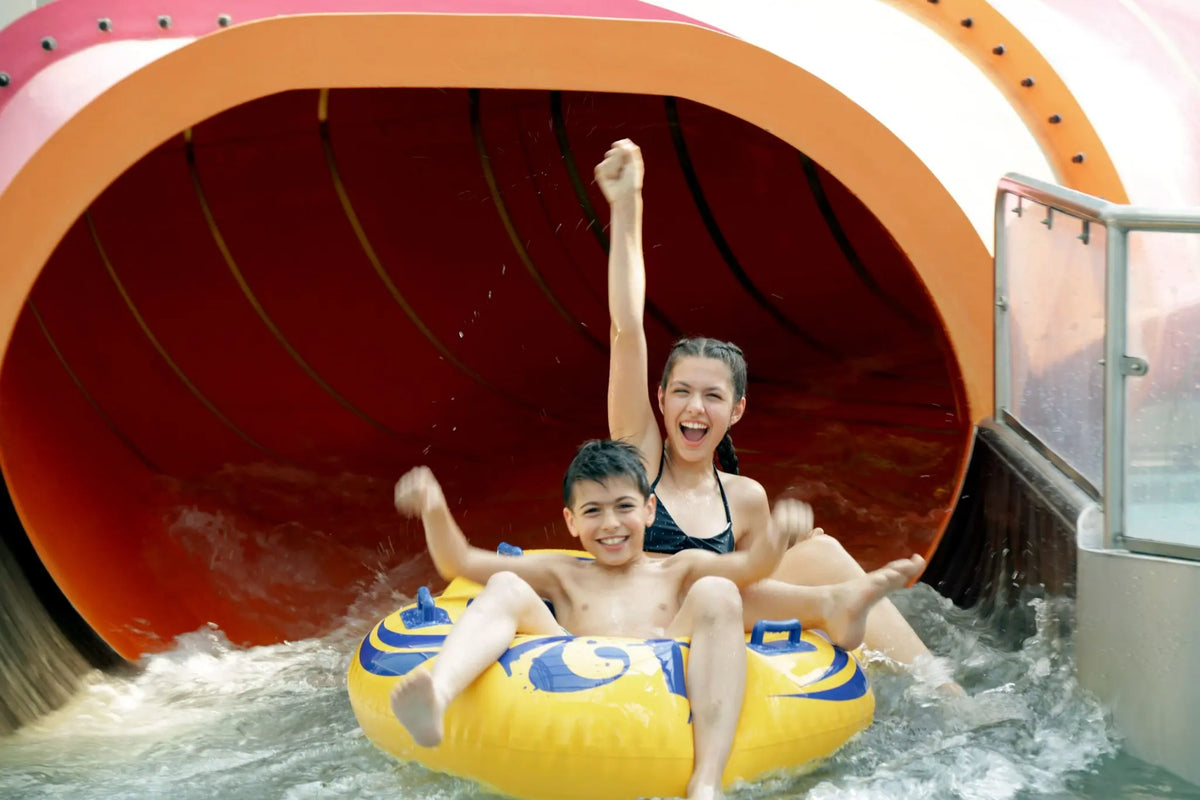 Zwei Kinder rutschen lachend in einem gelben Reifen aus einer großen Wasserrutsche im AQUALAND Köln