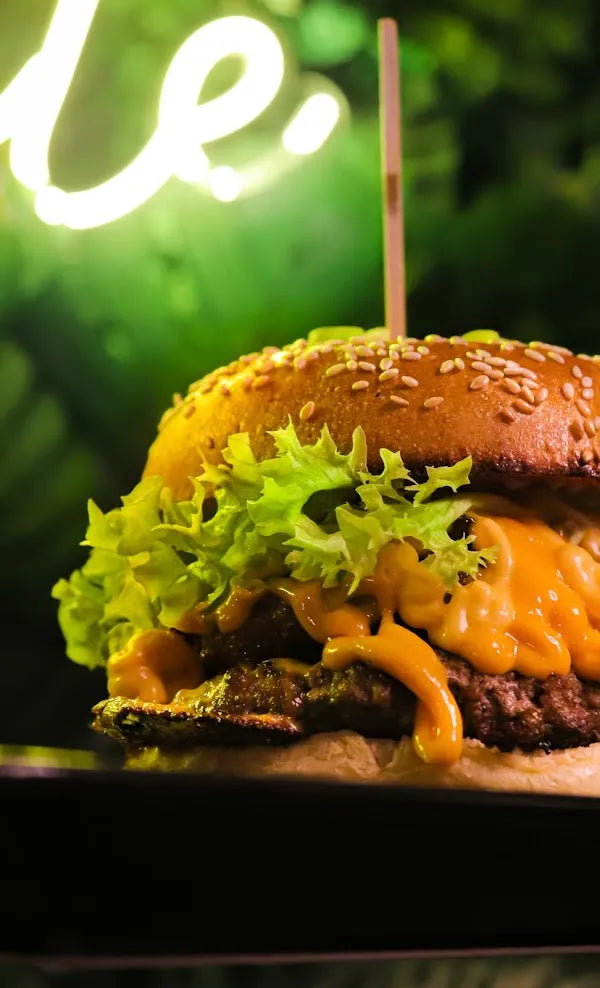 Nahaufnahme eines Cheeseburgers mit geschmolzenem Käse, grünem Salat und Sesambrötchen im stimmungsvollen Licht