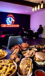 Tisch mit Chickenhood-Spezialitäten im Vordergrund und Gäste im Innenbereich