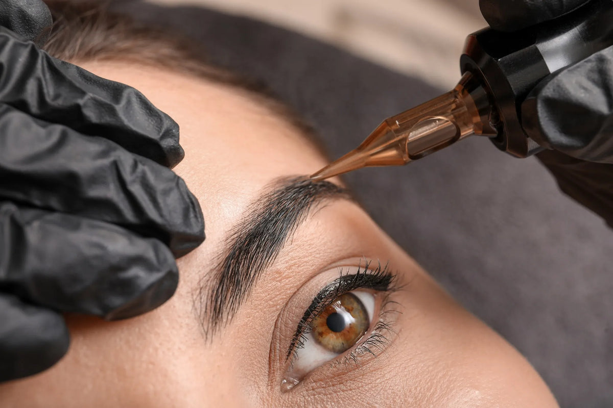 Nahaufnahme einer Augenbrauen-Pigmentierung mit Permanent-Make-up-Gerät durch eine Kosmetikerin mit schwarzen Handschuhen