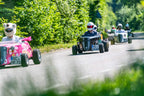 Teilnehmer der Hotrod Tour Aachen fahren mit Mini-Hotrods auf einer Landstraße bei sonnigem Wetter durch grüne Umgebung