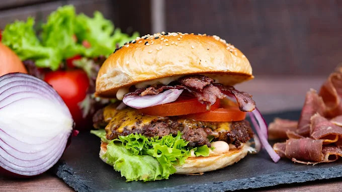 Saftiger Bacon-Cheeseburger mit Salat, Tomate, Zwiebeln und Käse im Sesambrötchen