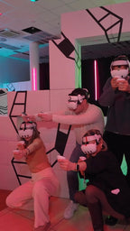 Gruppe von vier Personen spielt gemeinsam VR-Laser-Tag hinter Deckung in einer stylischen Arena in Berlin.