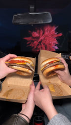 Zwei Personen halten je einen Burger vor der Leinwand im Autokino Essen, während der Film im Hintergrund läuf