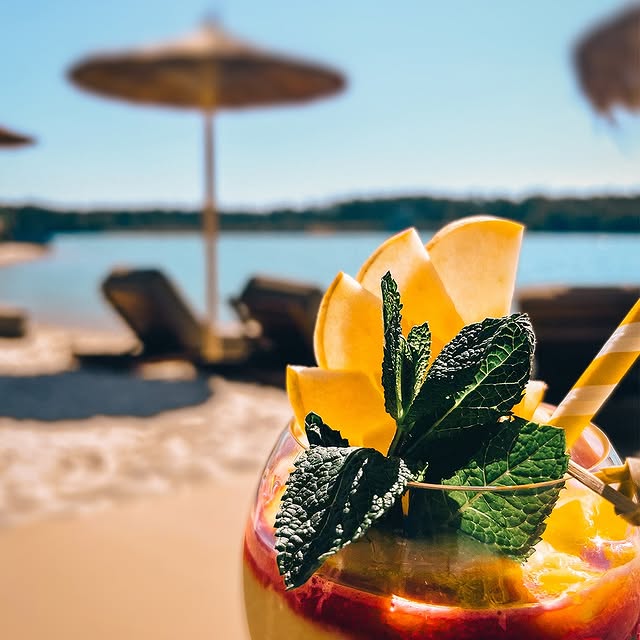Fruchtiger Cocktail mit Minze und Apfel-Deko am Sandstrand vom Chamäleon am See in Raunheim, im Hintergrund Liegen und Sonnenschirme
