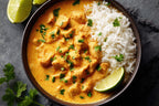 Cremiges indisches Chicken-Curry mit Basmatireis, frischem Koriander und Limette, serviert in einer Schale auf dunklem Untergrund.