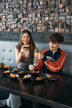 Junges Paar genießt verschiedene Tapas und Drinks in einem Restaurant mit moderner Holzwand-Deko. Auf dem Tisch stehen mehrere kleine Teller mit verschiedenen Gerichten und Getränken