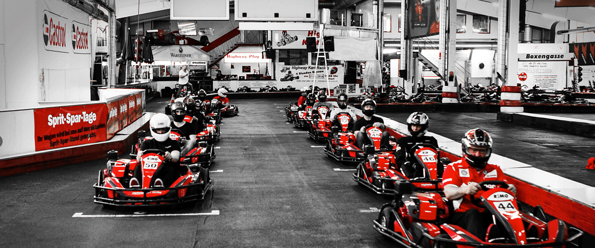 Mehrere Fahrer in roten Karts beim Start auf der Indoorbahn von Highway Kart Racing Dortmund