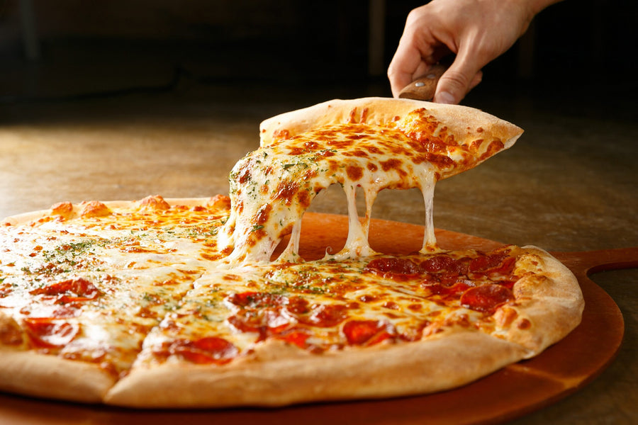 Frisch gebackene Pizza mit Käse und Salami, ein Stück wird mit ziehendem Käse abgehoben
